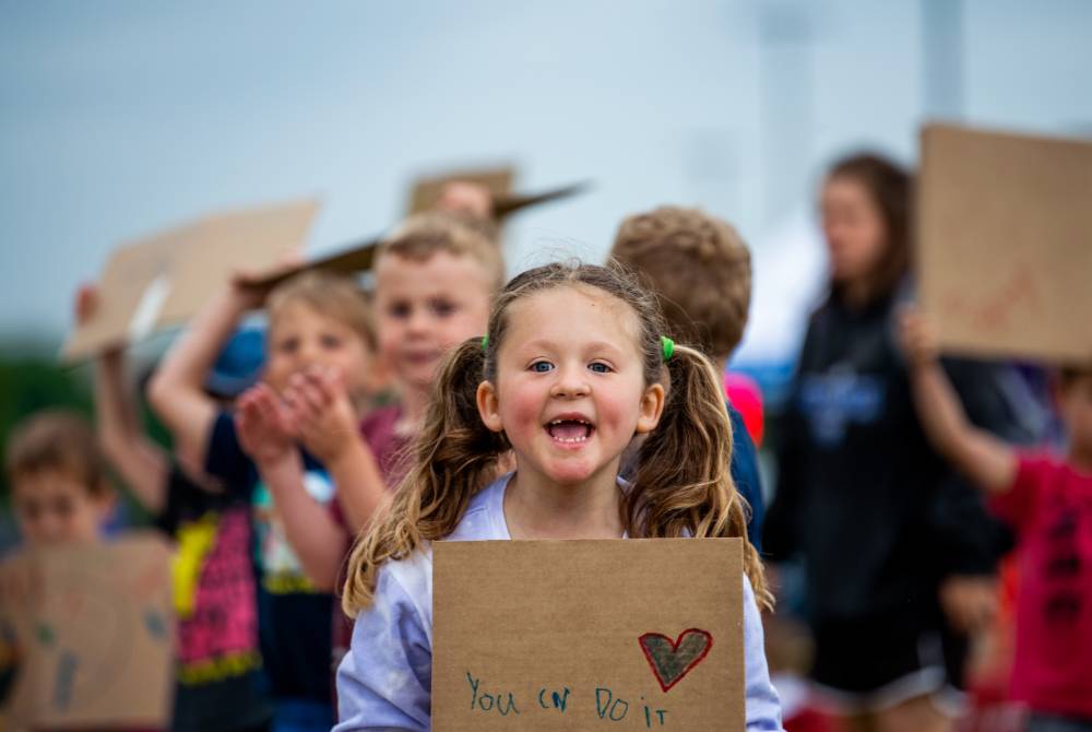 Young girl from the GVSU Children's Enrichment Center smiling and holding a handmade sign that reads "You can do it"
